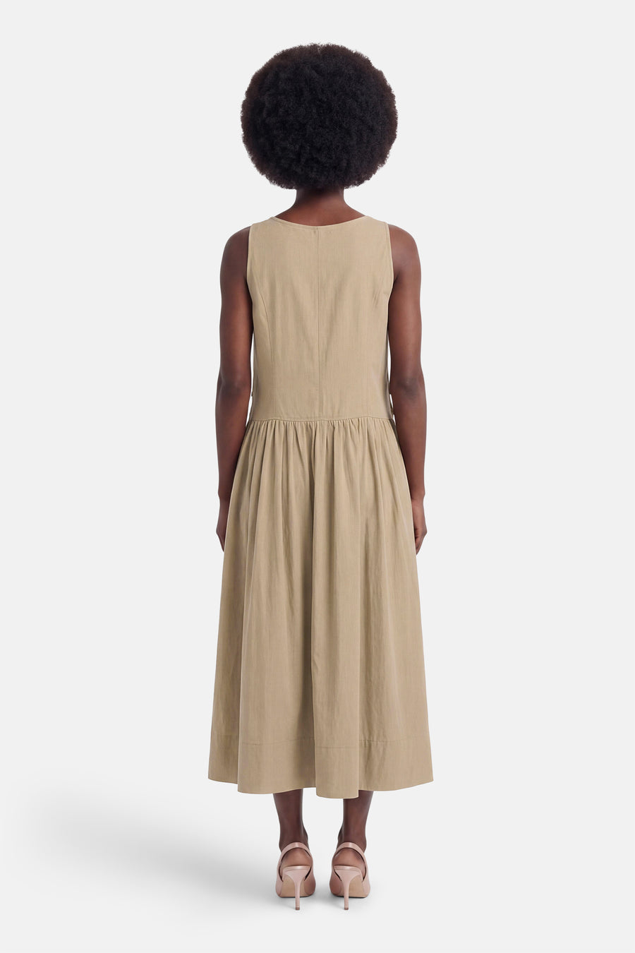 Beige mouwloos jurkje van ADORE, achterzijde met ruches en volle rok, model met afro kapsel en hoge hakken