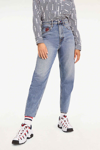 Femme en tenue Tommy Jeans, chemise rayée, jeans bleus et baskets blanches avec des accents rouges.