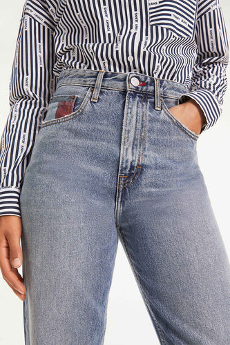 Photo de produit : un modèle porte un t-shirt rayé de la marque 'Tommy Jeans' et un jean bleu avec une main dans la poche.