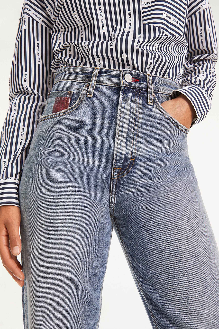 Photo de produit : un modèle porte un t-shirt rayé de la marque 'Tommy Jeans' et un jean bleu avec une main dans la poche.