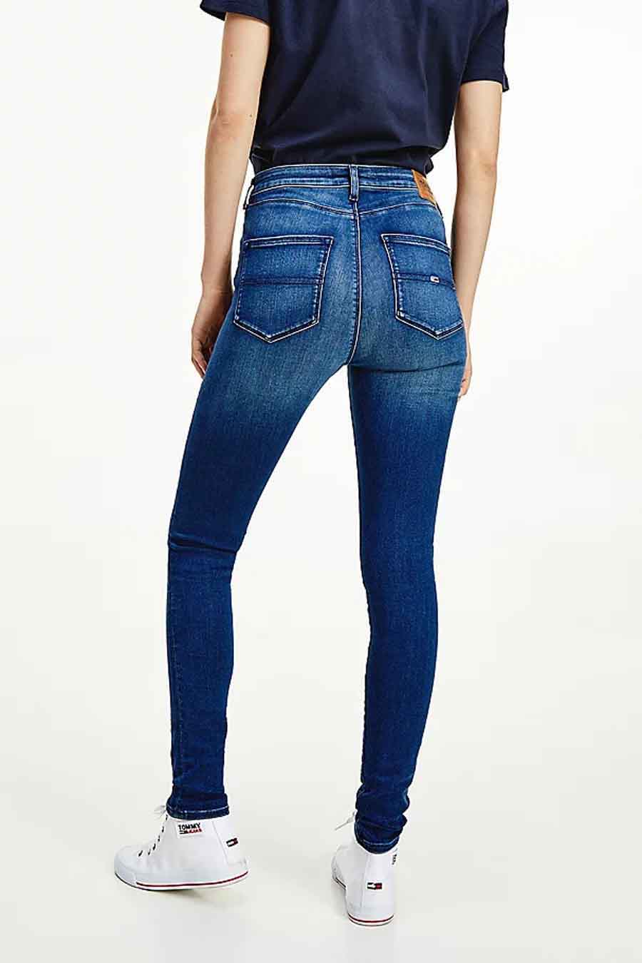 Donkerblauwe skinny jeans van TOMMY JEANS, met stiksels op de achterzakken en gedragen met witte sneakers.
