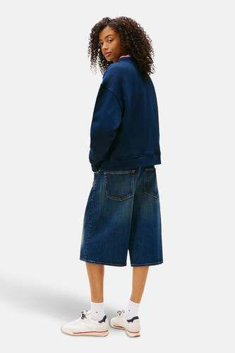 Pull-over bleu de TOMMY JEANS, porté avec des bermudas en denim et des chaussettes blanches avec des baskets.