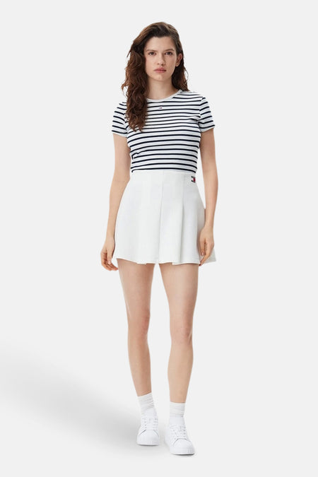 T-shirt bleu rayé à manches courtes de TOMMY JEANS, porté avec une jupe blanche et des baskets blanches.