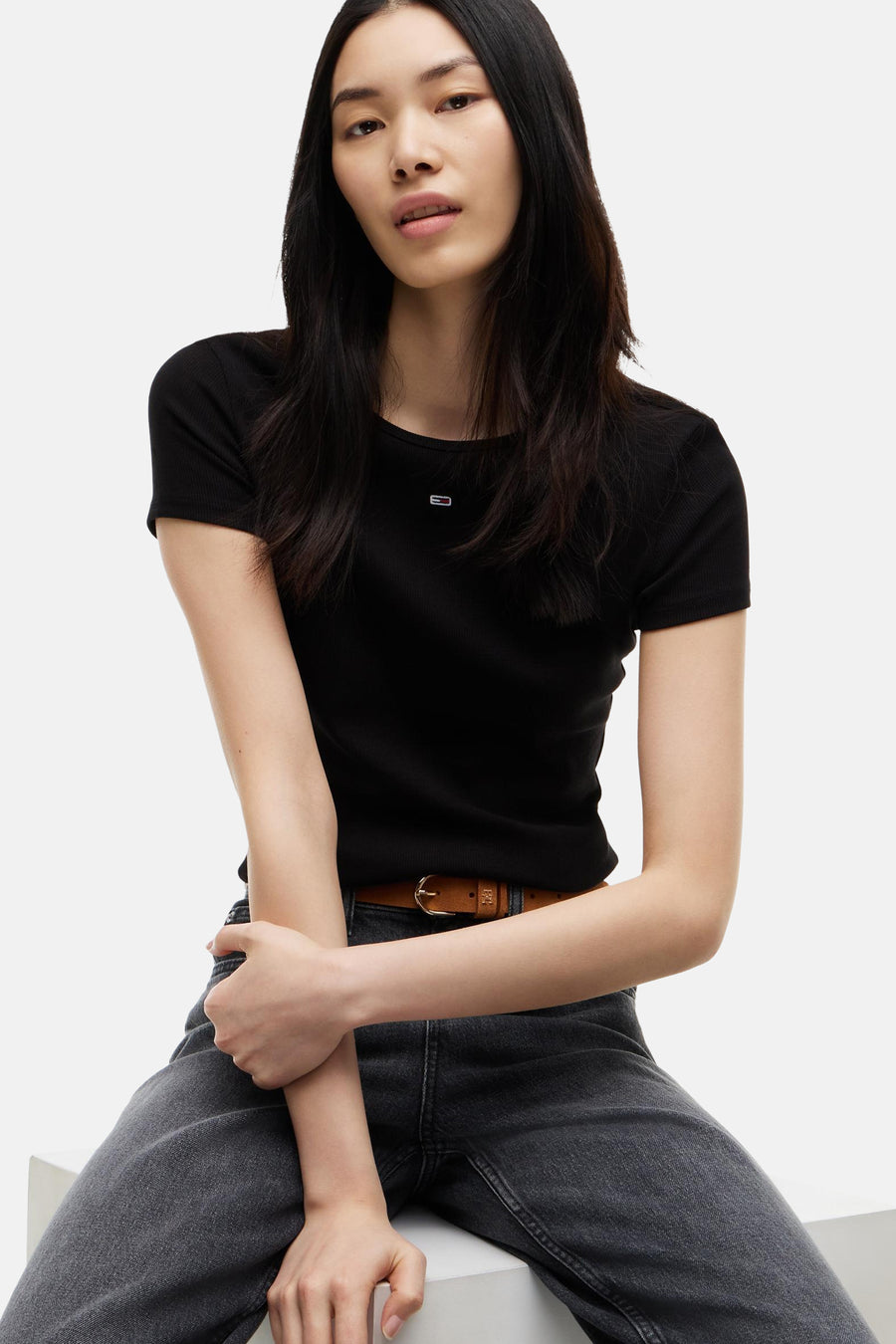 Zwart korte mouwen T-shirt van TOMMY JEANS, ribbeltextuur, klein logo op borst, model zit met donkere jeans en bruine riem