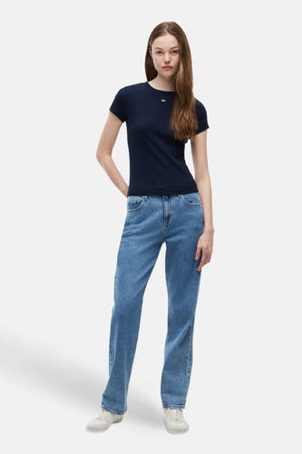 T-shirt bleu de TOMMY JEANS avec petit logo blanc, porté avec un jean bleu et des baskets blanches.