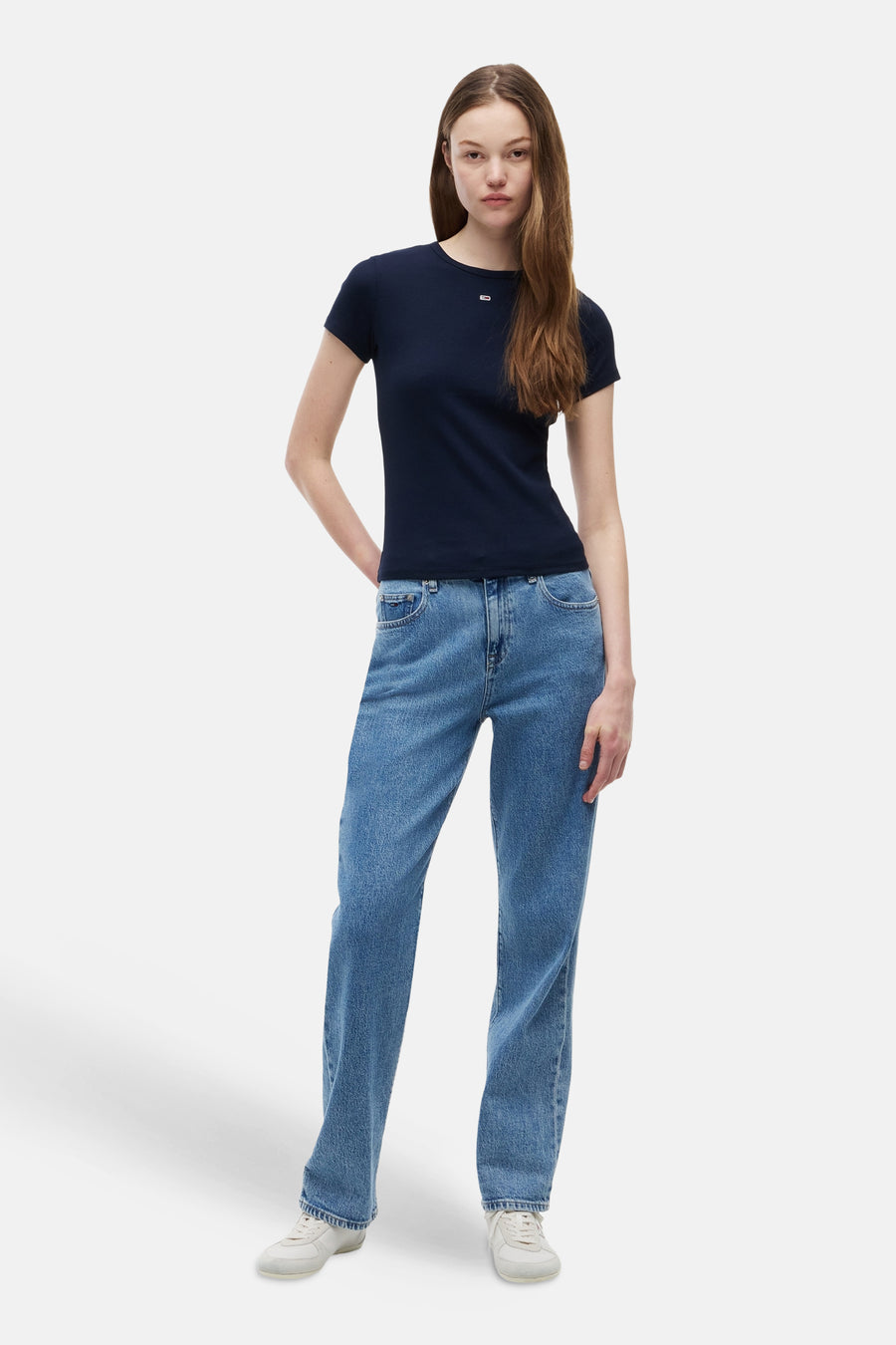 T-shirt bleu de TOMMY JEANS avec petit logo blanc, porté avec un jean bleu et des baskets blanches.
