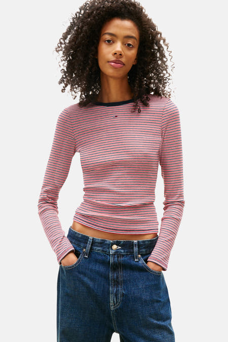 T-shirt multicolore à manches longues de TOMMY JEANS, avec un motif rayé, associé à des jeans larges et une sacoche brune.