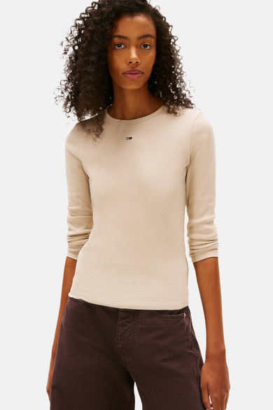 T-shirt beige à manches longues de TOMMY JEANS, avec un pantalon foncé et une chemise à carreaux autour de la taille.