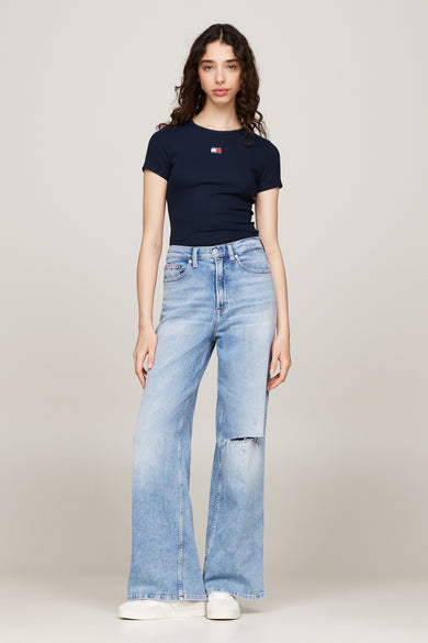 T-shirt bleu à manches courtes de TOMMY JEANS, porté avec un jean ample bleu clair déchiré et des baskets blanches.