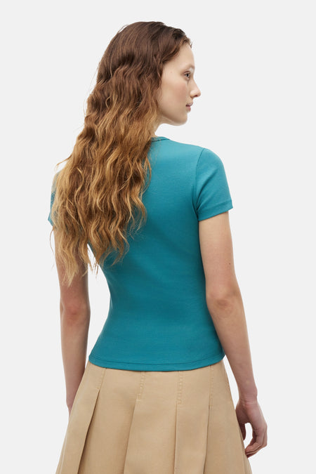 T-shirt vert côtelé vert de TOMMY JEANS, à manches courtes, porté de dos par un mannequin sur une jupe beige.