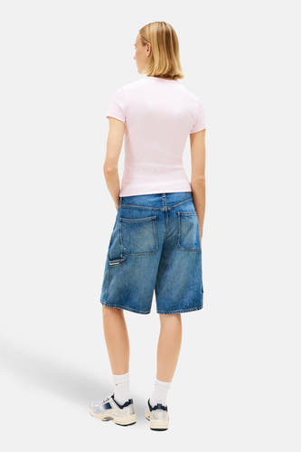 T-shirt rose à manches courtes de TOMMY JEANS, avec un style décontracté et porté avec un short en jean bleu et des baskets blanches.