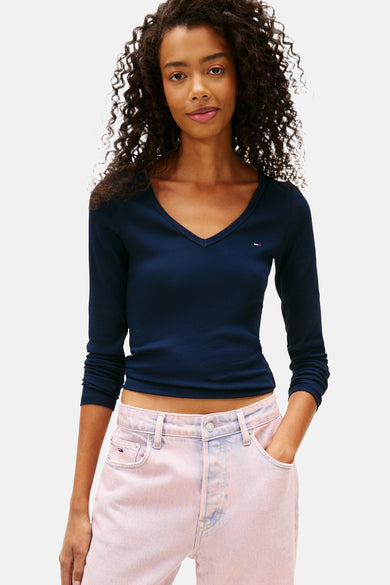 T-shirt bleu à manches longues de TOMMY JEANS, avec col V, associé à des jeans roses et un pull autour de la taille.