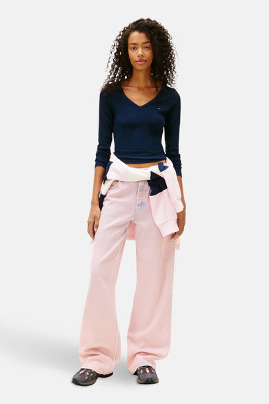 Blauw T-shirt met lange mouwen van TOMMY JEANS, met V-hals, gecombineerd met roze jeans en een sweater om de taille.