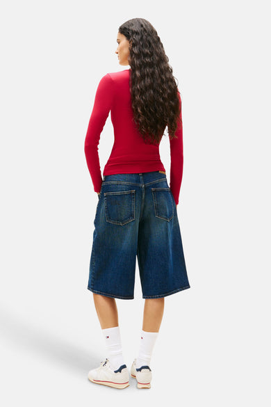 T-shirt rose à manches longues de TOMMY JEANS, porté avec des bermudas en denim et des chaussettes blanches avec logo.