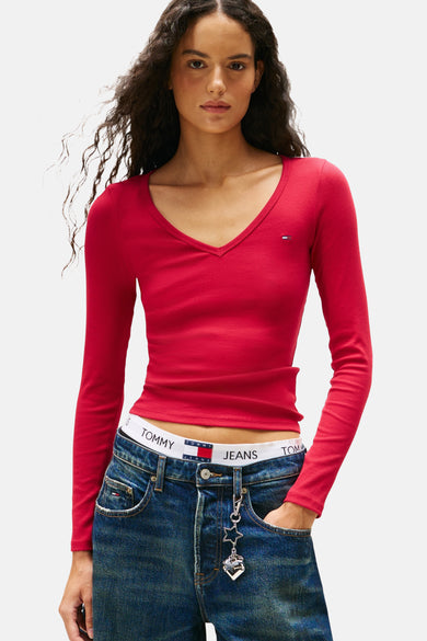 T-shirt rose à manches longues de TOMMY JEANS, avec un col V et porté avec un jean à une bande blanche.