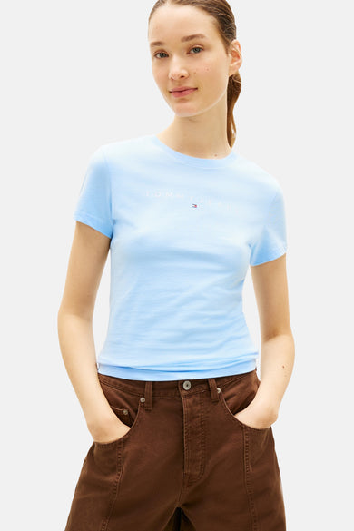 T-shirt bleu de TOMMY JEANS, porté avec un pantalon marron évasé et des baskets blanches.