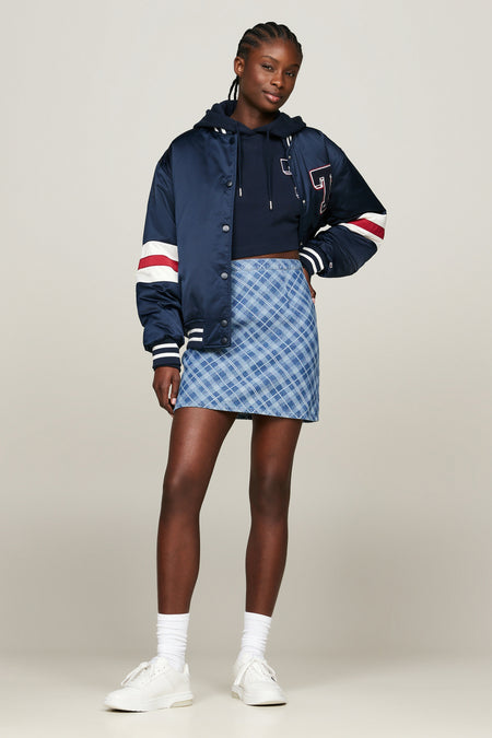 Jupe courte bleue de TOMMY JEANS avec motif à carreaux diagonaux bleu clair et petit logo sur la ceinture, portée avec un pull bleu foncé.