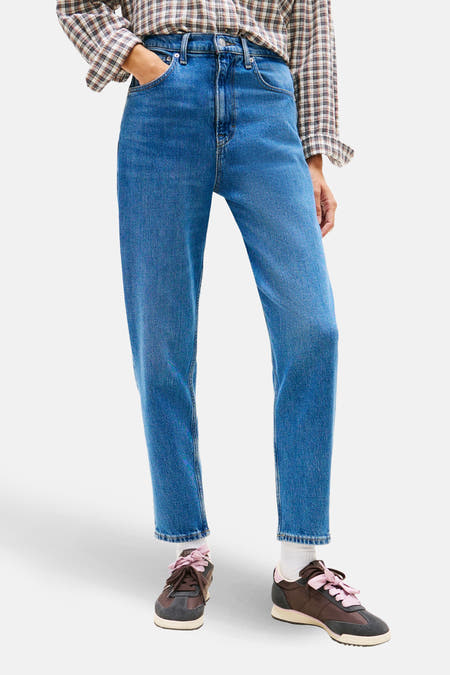 MOM JEANS in mid blue denim van TOMMY JEANS, gecombineerd met een geruite blouse en bruine sneakers.
