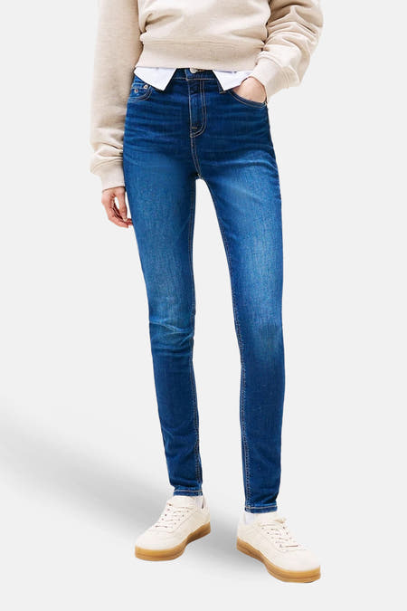 Jean skinny en denim bleu marine de TOMMY JEANS, avec un pull décontracté et des baskets.