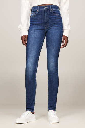 Jean skinny bleu marine de TOMMY JEANS, porté avec un pull tricoté blanc et des baskets blanches.