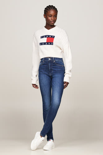 Donkerblauwe skinny jeans van TOMMY JEANS, gedragen met een witte gebreide trui en witte sneakers.
