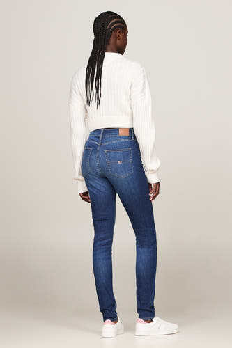 Jean skinny bleu marine de TOMMY JEANS, avec un pull blanc et des baskets blanches.