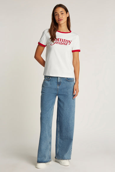 T-shirt blanc à manches courtes de Tommy Jeans, terminé avec des suries rouges le long du col et des manches, porté avec des jeans larges.