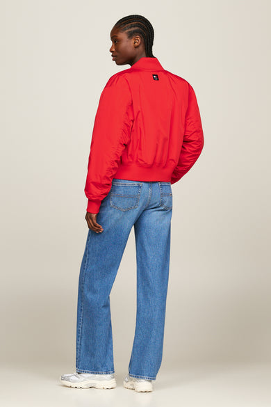 Veste rouge de TOMMY JEANS, avec des manches longues, portée avec des jeans larges et des baskets blanches.