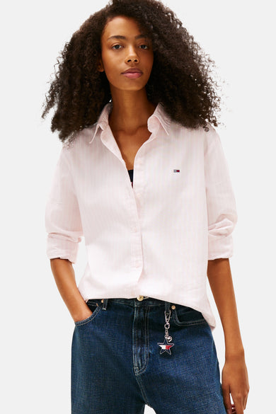 Chemise rose à manches longues de TOMMY JEANS, avec un motif rayé subtil, associée à des jeans larges et des chaussures décontractées.