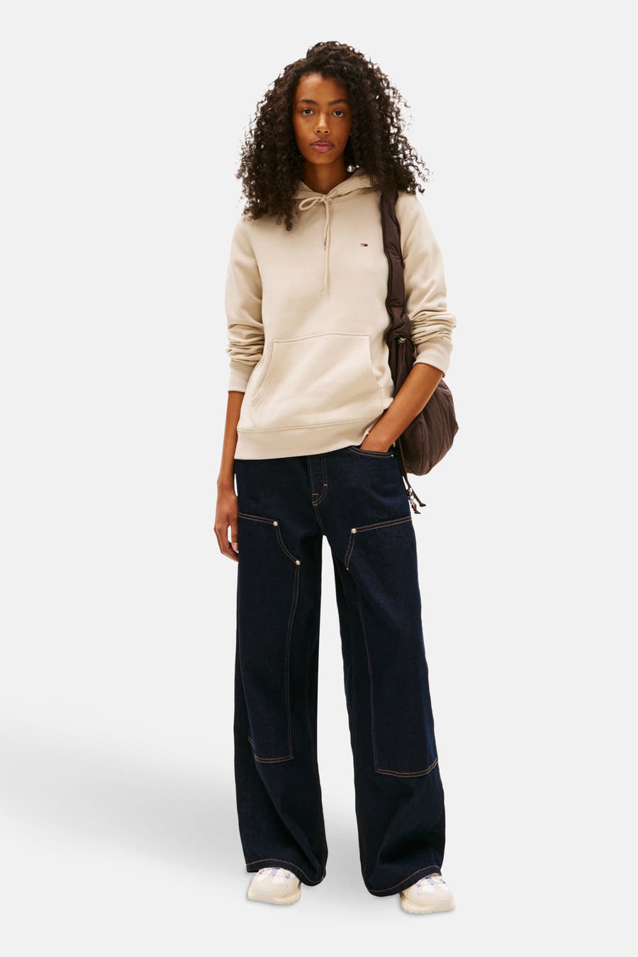 Beige sweater van TOMMY JEANS, gecombineerd met wijde jeans en een bruine tas.
