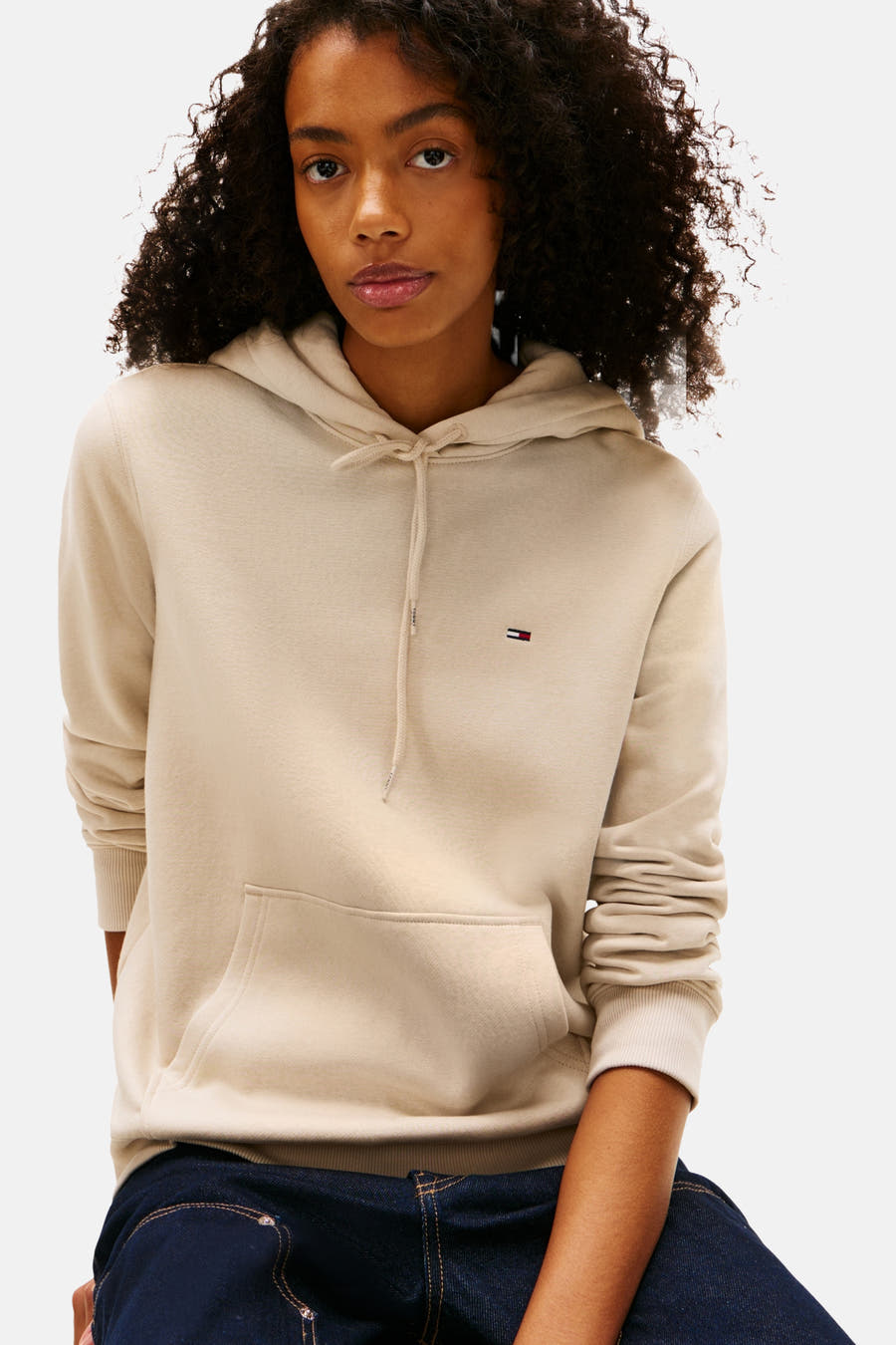 Gilet beige de TOMMY JEANS, avec capuche, longues manches et jeans bleu marine.