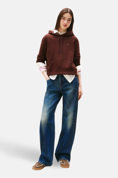 Pull-over marron avec col rond de TOMMY JEANS, porté sur un chemisier blanc et des jeans bleus larges et des chaussures marrons.