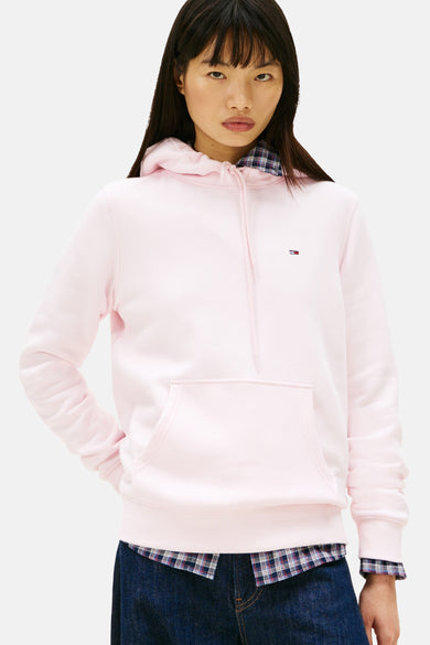 Pull-over rose de TOMMY JEANS, avec capuche et manches bouffantes, jeans bleu foncé et baskets brunes.