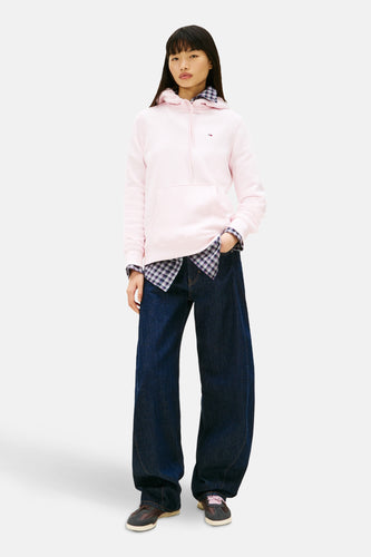 Vrouw in roze hoodie, geruite blouse, wijde jeans en sneakers.