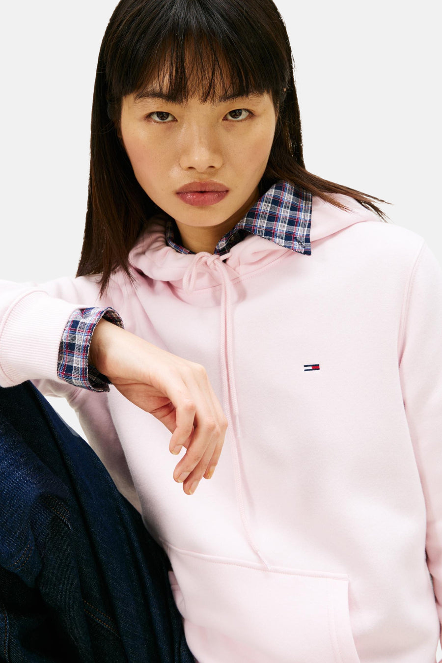 Jonge vrouw draagt een roze hoodie met een geruit overhemd eronder, en donkere spijkerbroek.