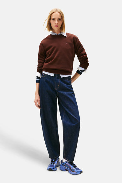 Pull-over marron de TOMMY JEANS, associé à un chemisier rayé et des jeans larges bleu marine avec des baskets bleues.