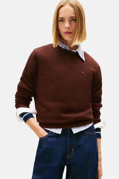 Pull-over marron de TOMMY JEANS, porté sur un chemisier rayé et avec des jeans bleus.
