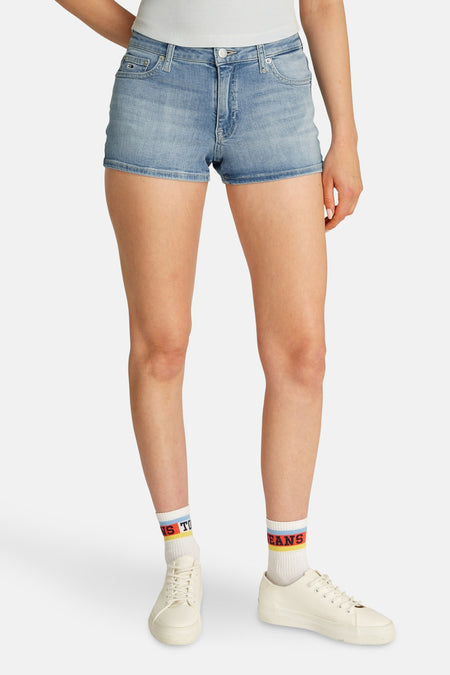 Shorts en denim bleu clair court de TOMMY JEANS, portés avec des baskets blanches et des chaussettes à rayures et imprimées.