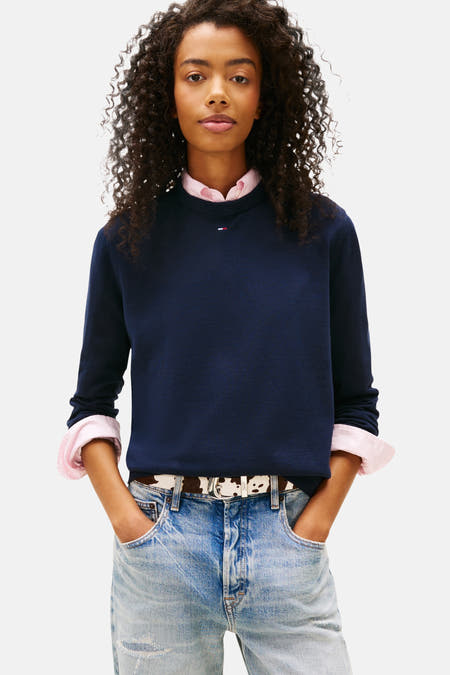 T-shirt bleu avec col rond de TOMMY JEANS, à longues manches, associé à une chemise rose, un pantalon de travail et des baskets blanches.
