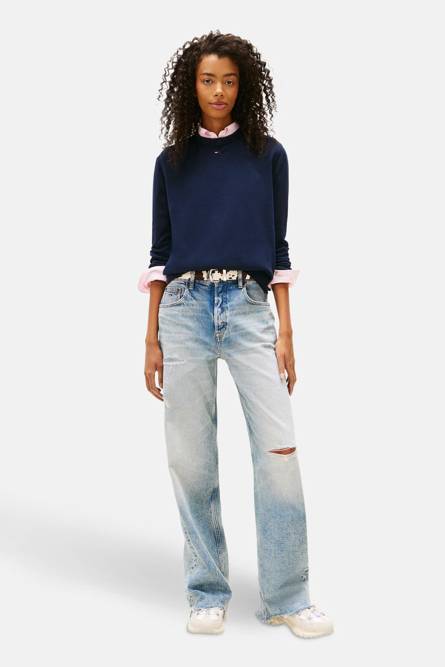 Blauwe trui met ronde hals van TOMMY JEANS, met lange mouwen, gecombineerd met een roze overhemd, een spijkerbroek en witte sneakers.