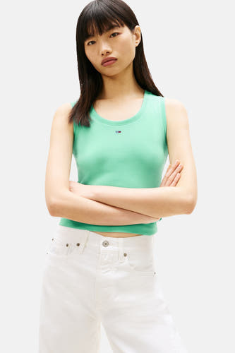 T-shirt vert à manches courtes TOMMY JEANS, porté avec un pantalon blanc et des baskets colorées.