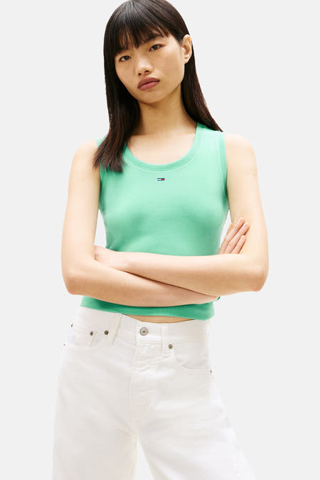T-shirt vert à manches courtes TOMMY JEANS, porté avec un pantalon blanc et des baskets colorées.