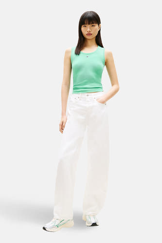 Groen T-shirt met korte mouwen van TOMMY JEANS, gedragen met witte broek en kleurrijke sneakers.
