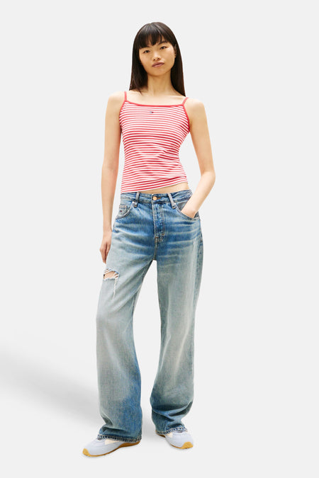 Multikleurige top van TOMMY JEANS met rode en witte strepen, gedragen met wijde jeans en sneakers.
