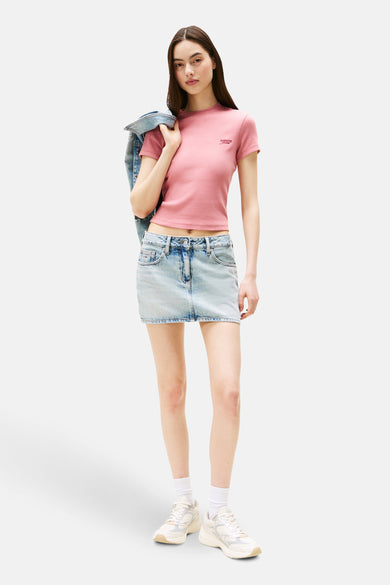 T-shirt rose à manches courtes de TOMMY JEANS, porté sur l'épaule avec un blouson en denim, et une jupe en denim.
