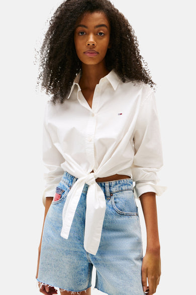 Chemise blanche à manches longues de TOMMY JEANS, boutonnée à l'avant, portée avec des shorts en denim.