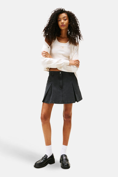 Jupe courte noire de TOMMY JEANS, associée à une chemise rayée et des loafers noirs avec des chaussettes blanches.