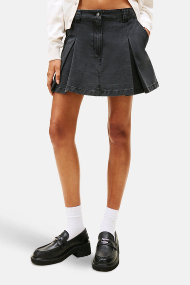 Jupe courte noire de TOMMY JEANS, style plié, associée à des chaussettes blanches et des loafers noirs.