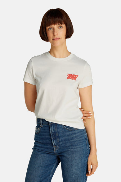 T-shirt blanc à manches courtes de TOMMY JEANS, avec logo rouge sur la gauche et associé à des jeans bleus.