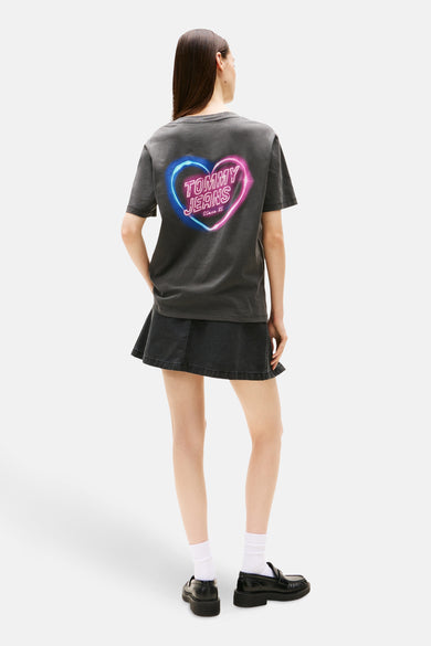 T-shirt gris à manches courtes de Tommy Jeans, avec un imprimé en forme de cœur sur le dos, associé à une jupe sombre.